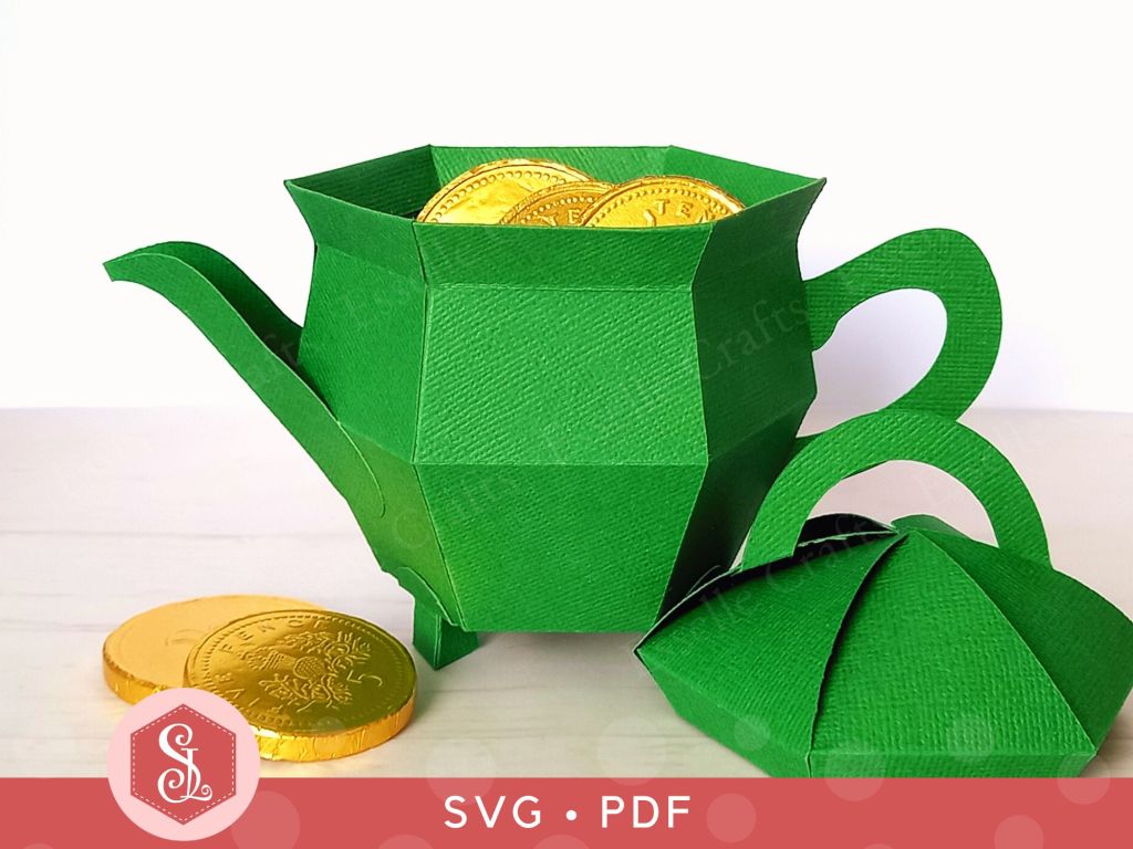 A green papercraft teapot gift box in the shape of a St Patricks Day pot of gold. The lid is off, showing the box is filled with gold chocolate coins.