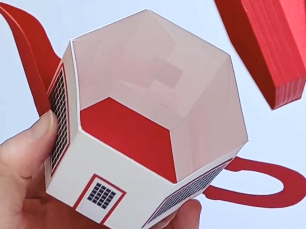 A small papercraft teapot gift box made in the style of the teapot dome gas station with a white body a red lid a red handle and spout and tiny black windows