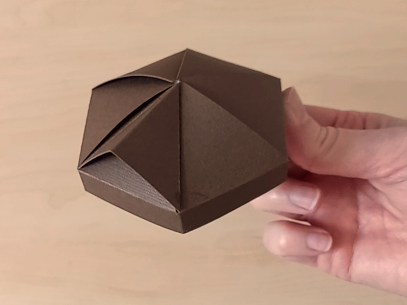 The hexagonal lid of a 3D paper craft teapot gift box made in the style of a cosy country cottage