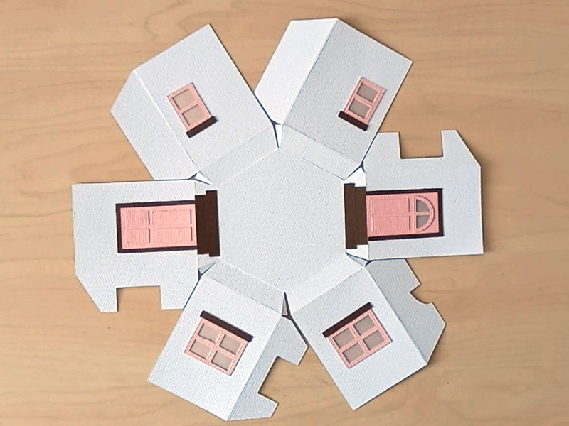 A 3D paper craft teapot gift box made in the style of a cosy country cottage with pink doors and pink windows