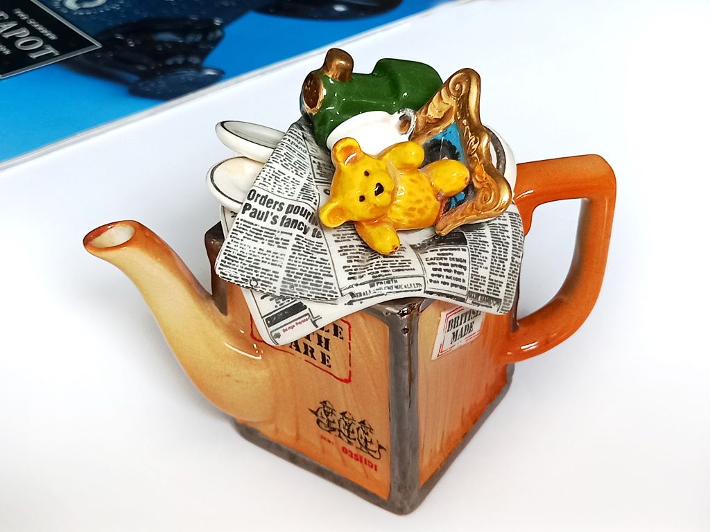 A one cup novelty teapot designed to look like a wooden tea chest with a small teddy bear and newspapers as the teapot lid
