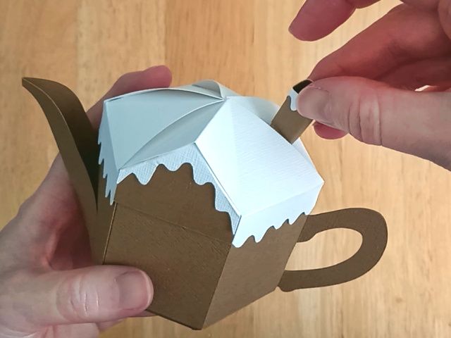 A brown paper craft teapot gift box in the style of a classic gingerbread house
