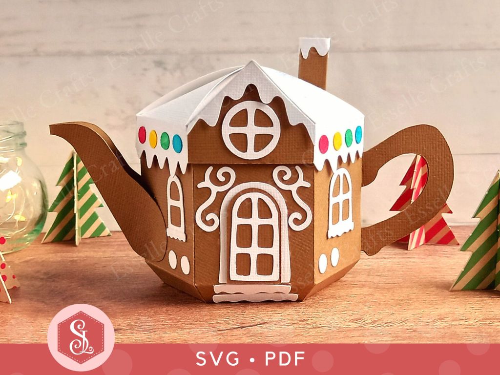 A brown paper craft teapot gift box in the style of a classic gingerbread house with a white icing lid white icing door and windows and white icing swirls