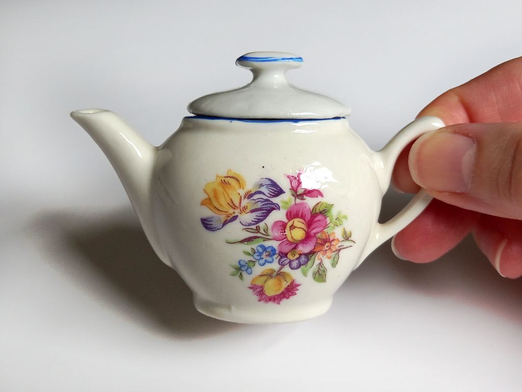 A small white ceramic teapot decorated with delicate summer flowers from a childs vintage tea set
