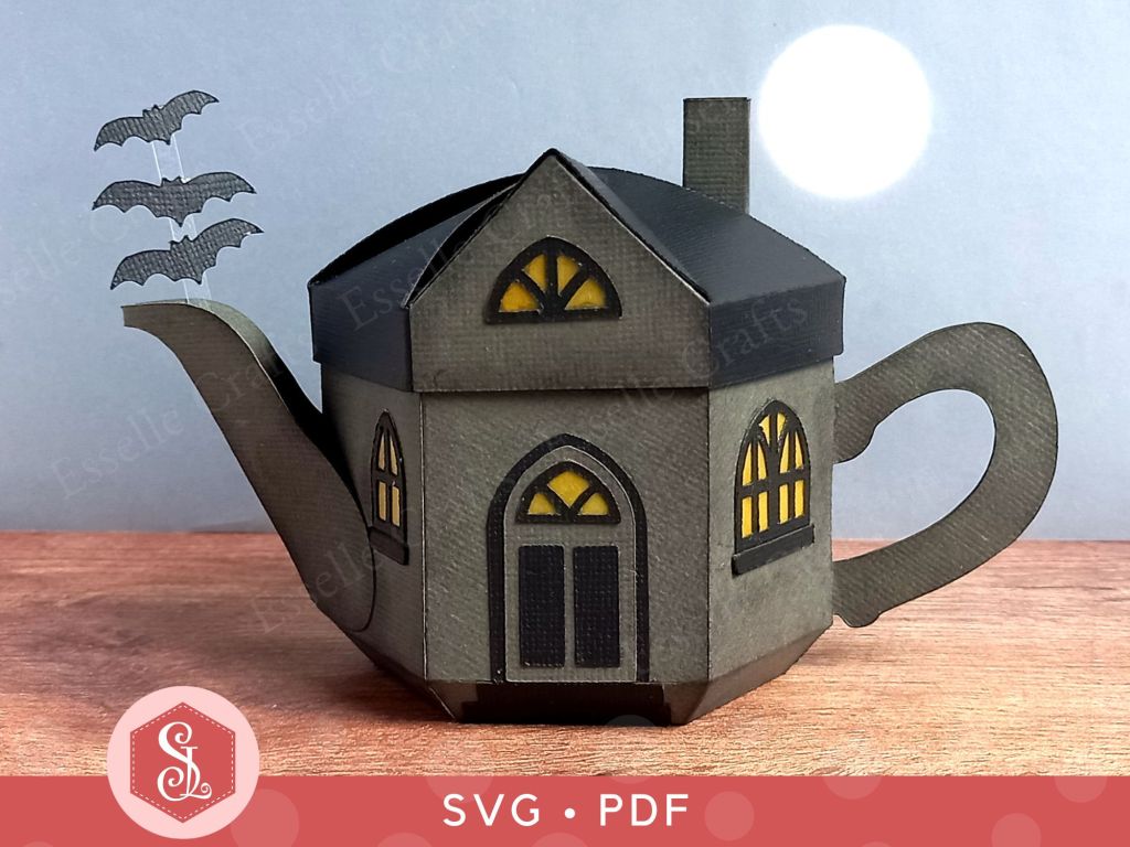A paper craft haunted house gift box for Halloween trick or treating in the shape of a teapot with yellow arched gothic windows and three bats flying out of the spout