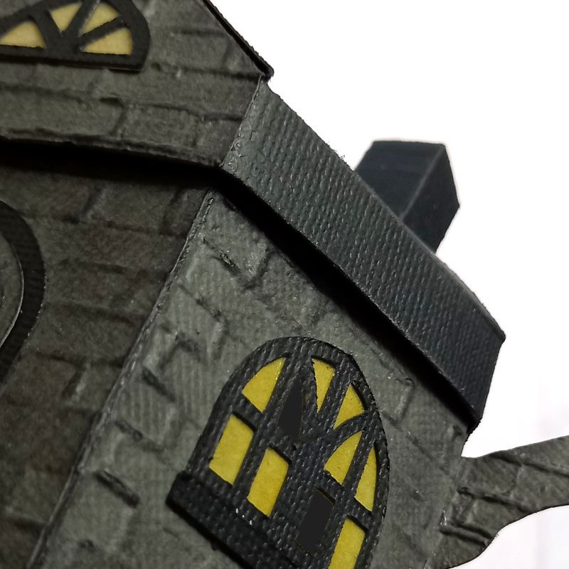 A paper craft haunted house gift box for Halloween trick or treating in the shape of a teapot with yellow arched gothic windows