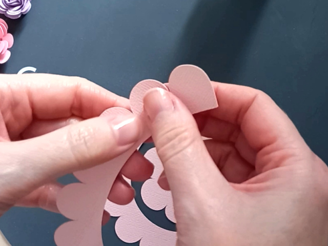 Starting to make a pink rolled paper flower by gently curling the paper into shape