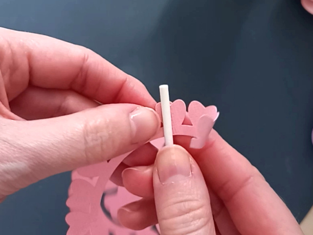 Starting to make a pink rolled paper flower by gently curling the petals into shape using a thin lollipop stick