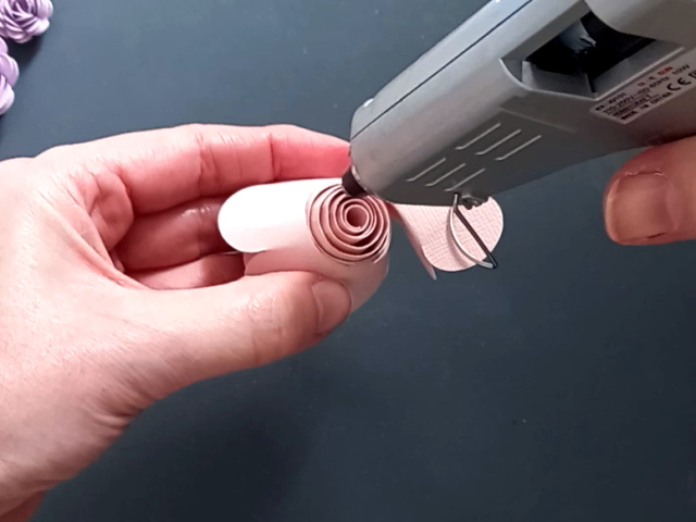 Applying hot glue to the centre of a pink rolled paper flower to hold it in place