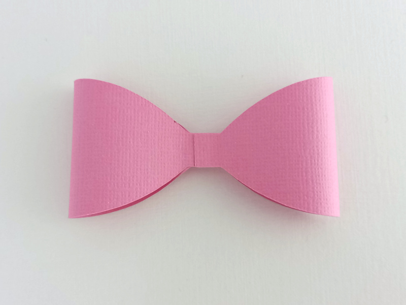 A pink butterfly bow made from textured cardstock that can be used on gift packaging or home decor