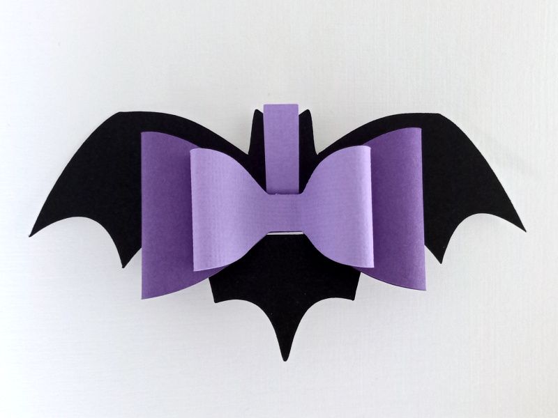 A black and purple bat bow made from textured cardstock that can be used on Halloween gift packaging or home decor