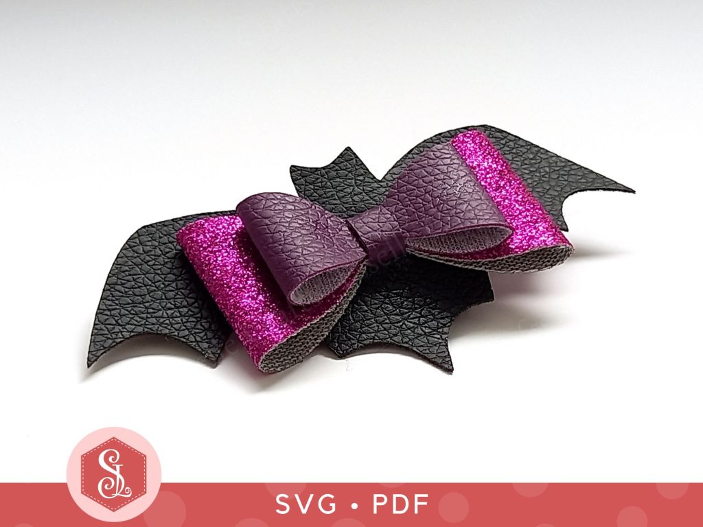 A black and purple bat bow made from faux leather and thin glitter fabric that can be used as a Halloween hair bow or a brooch