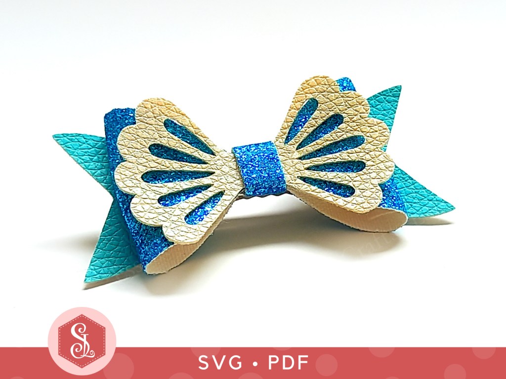 A mermaid hair bow made from blue glitter fabric and teal and cream faux leather that can be used on a hair clip or worn as a brooch
