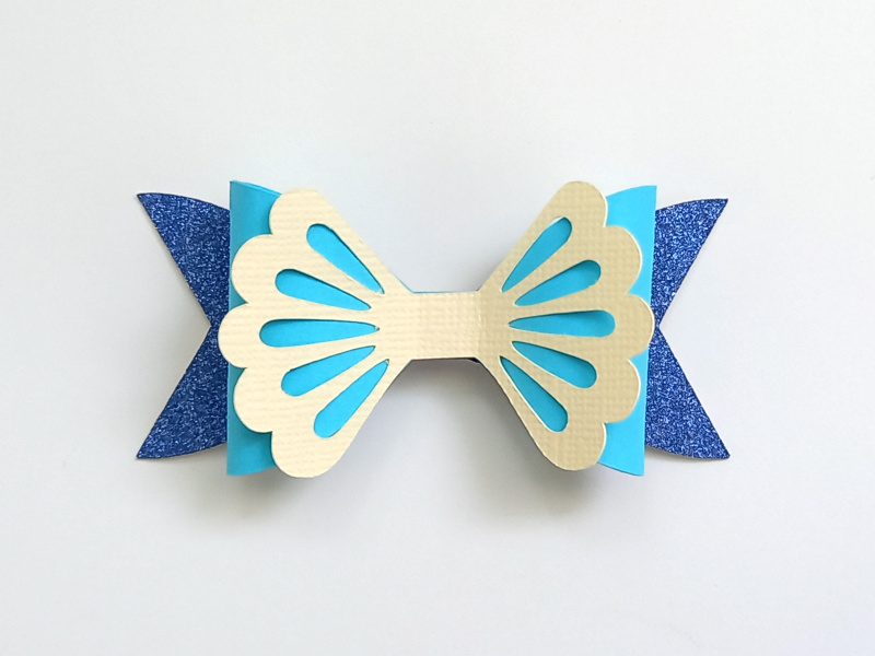 A mermaid gift bow made from blue glitter cardstock and teal and cream cardstock that can be used on gift packaging or home decor