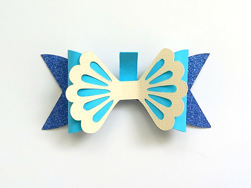 A mermaid gift bow made from blue glitter cardstock and teal and cream cardstock that can be used on gift packaging or home decor