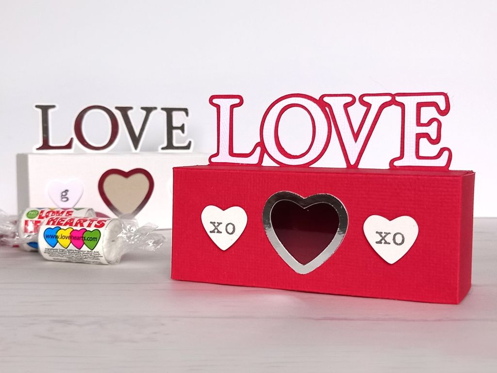 A red papercraft treat box for Valentine's day with the word LOVE on the top and decorated with paper hearts