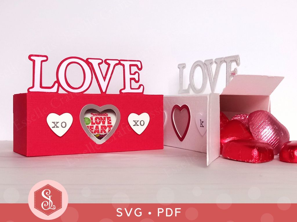 A red papercraft treat box for Valentine's day with the word LOVE on the top and decorated with paper hearts
