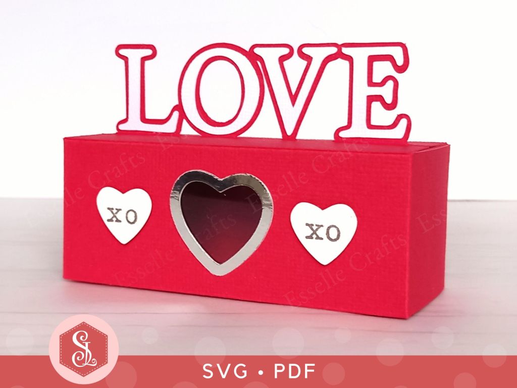 A red papercraft treat box for Valentine's day with the word LOVE on the top and decorated with paper hearts
