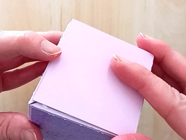 A papercraft favour box in the style of a flower made from lavender paper and closed with a satin ribbon