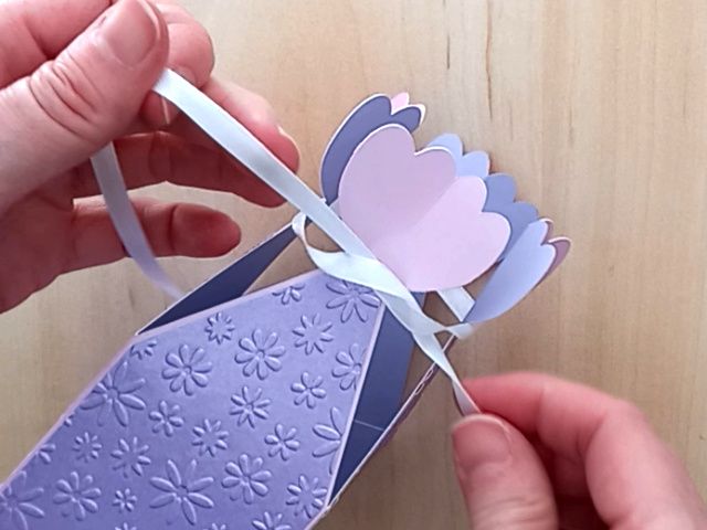 A papercraft favour box in the style of a flower made from lavender paper and closed with a satin ribbon