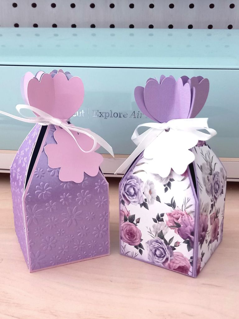 Two papercraft favour boxes in the style of a flower made from lavender paper and closed with a satin ribbon