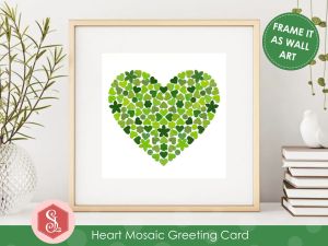A square greeting card with a green mosaic heart design on the front made from small pieces of upcycled paper packaging. The card is displayed in a square frame on a shelf. 