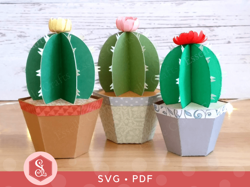 Three papercraft favour boxes in the shape of a cactus in a plant pot with colourful paper flowers on the top