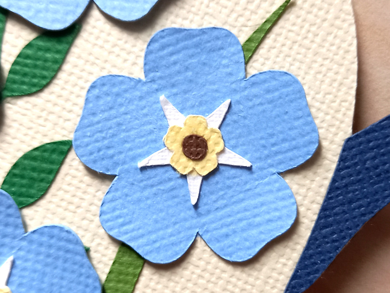 A papercraft forget-me-not flower on a cream background.
