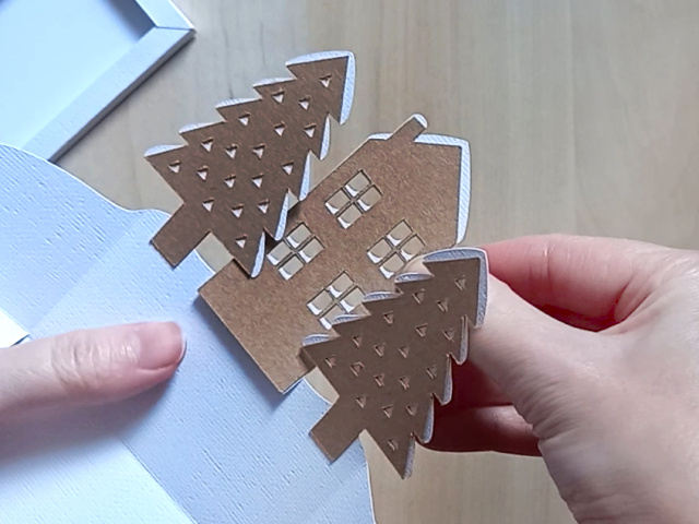 A Christmas countdown advent calendar, which comes as a DIY papercraft template, featuring a central house, two pine trees, and two numbered blocks that double up as gift boxes. It can be refilled and reused each year.