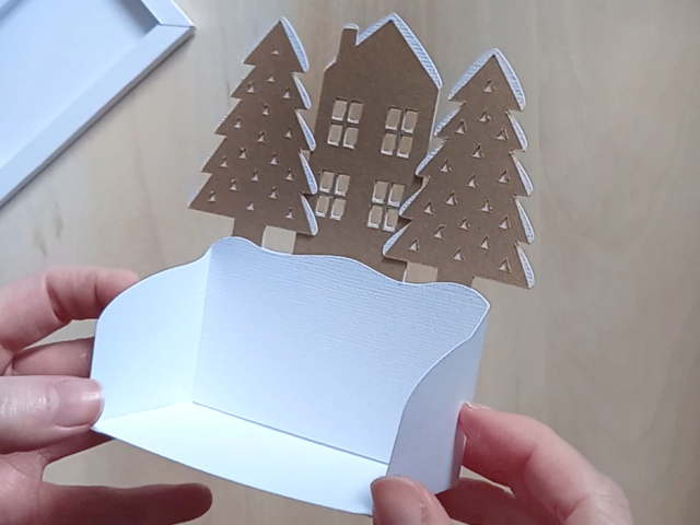 A Christmas countdown advent calendar, which comes as a DIY papercraft template, featuring a central house, two pine trees, and two numbered blocks that double up as gift boxes. It can be refilled and reused each year.