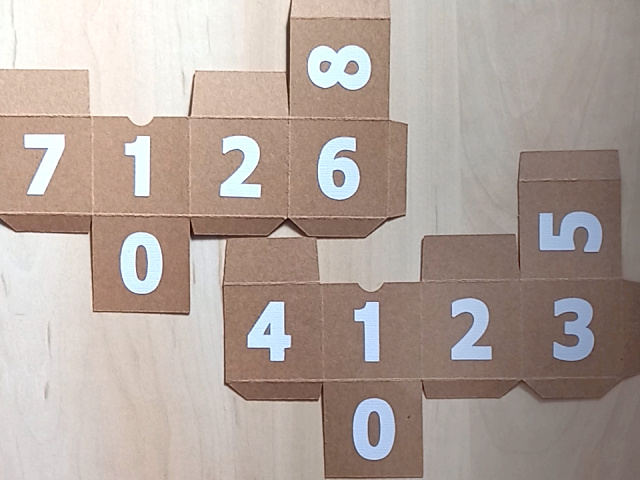 A Christmas countdown advent calendar, which comes as a DIY papercraft template, featuring a central house, two pine trees, and two numbered blocks that double up as gift boxes. It can be refilled and reused each year.