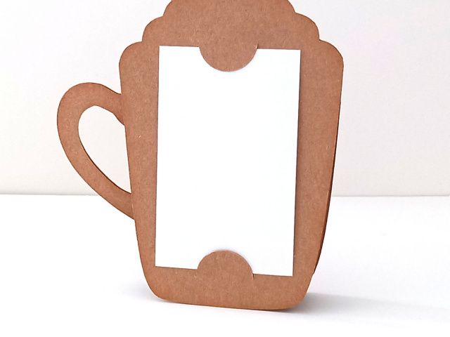The back view of a papercraft gift card holder in the style of a pumpkin spice latte mug. It is holding a plain white piece of card for a handwritten message.